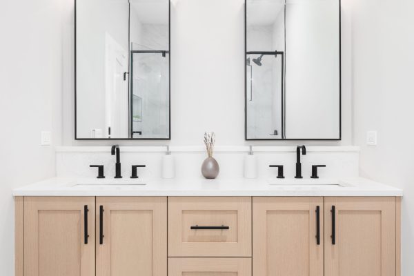 A modern bathroom with a wooden vanity cabinet, black faucets, white marble countertop, and black rimmed square mirrors.